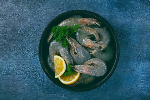 Fresh raw white-footed shrimp, tiger prawns vannamey, on a clay plate, with lemon and herbs, on a