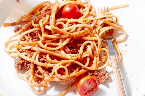 A plate holds freshly cooked spaghetti topped with flavorful meat sauce and garnished with bright
