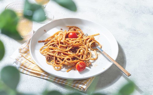 A plate of perfectly cooked spaghetti is topped with rich sauce and fresh tomatoes. Next to it, a