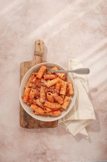 Rigatoni pasta with meat sauce and parmesan cheese on a light table, top view, homemade, no people