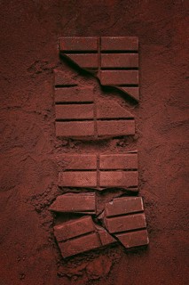Chocolate bars broken and scattered on cocoa powder background with rich texture and color