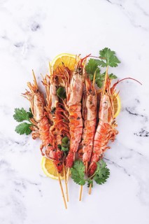 Shrimps on skewers, Grilled, spread on a marble surface, garnished with lemon slices and fresh