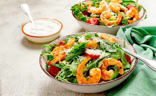 Two bowls of shrimp salad, arugula and cherry tomatoes, with parmesan cheese, healthy food