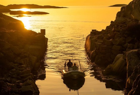 Motorboat with two persons sailing in harbour entrance at sunset, archipelago, Smögen,