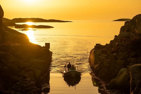 Motorboat with two persons sailing in harbour entrance at sunset, archipelago, Smögen,