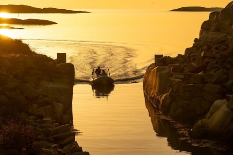 Motorboat with two persons sailing in harbour entrance at sunset, archipelago, Smögen,