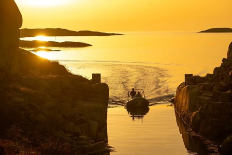 Motorboat with two persons sailing in harbour entrance at sunset, archipelago, Smögen,