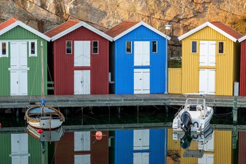 Colourful boathouses and boats in the calm water in front of rocks in the harbour of Smögen,