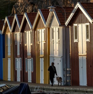 Woman with dog in front of colourful boathouses in the harbour of Smögen, Smögenbryggan, Västra