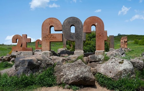 Stone pillars with traditional motifs, surrounded by large rocks and green grass, monument to the