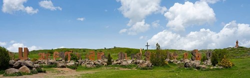 Wide landscape with rocks and a cross, surrounded by green meadow and blue sky, monument of the