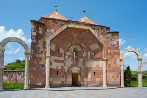 Front view of a stone church with striking arches and three crosses on the roof, Saint Trinity