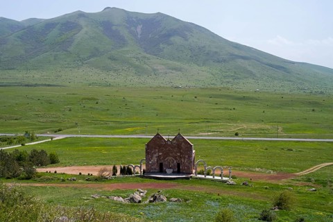 Small stone church in a vast green landscape in front of a mountain with clouds, Saint Trinity