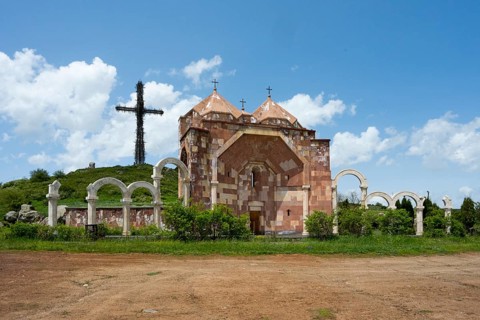 Stone architecture church with arches and cross on a hill under a cloudy blue sky, Monument of the