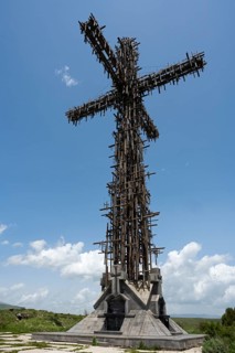 High metal cross with complex structure under a blue sky with clouds, Monument of the Holy Cross,