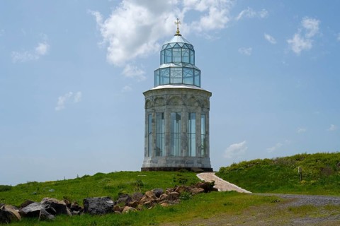 Glass church on a hill path, crowned by a golden cross under a cloudy sky, Garden of Eternity,