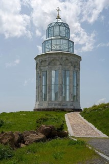 Glass church with decorative cross in a meadow under a blue sky, Garden of Eternity, Aparan,