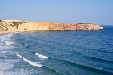 Cliffs with the Hotel Pousada de Sagres and surfers in the sea, Praia da Mareta, Sagres, Algarve,