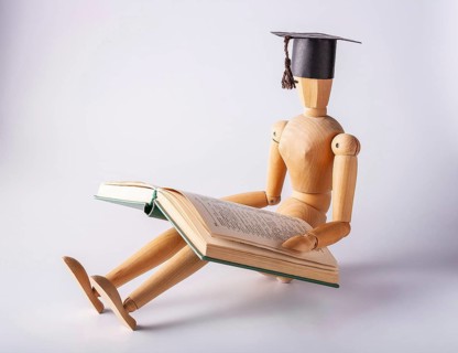 Wooden man in a student cap sits on the floor and reads a book, copy space