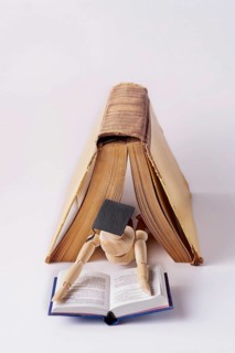 A wooden man in a student cap lies under an open book and reads a textbook, space for text