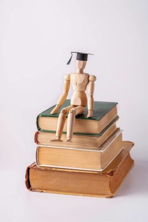 A wooden man in a student cap sits on a stack of textbooks on a white background