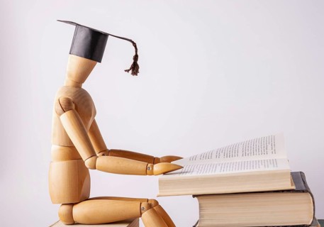 A wooden man in a student cap is reading a book