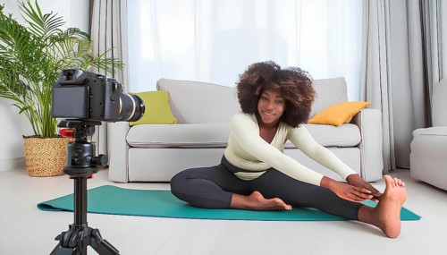 A woman is doing a yoga pose in front of a camera. The camera is on a tripod and is recording her