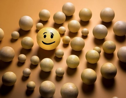 Wooden balls feature faces, one smiling among sad expressions, representing positivity or