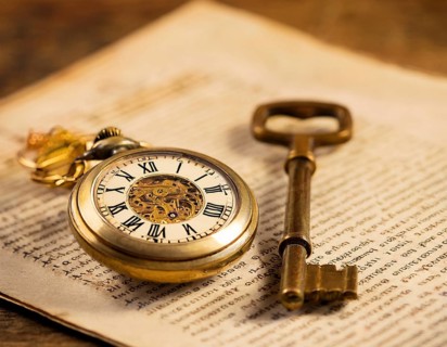 A classic golden pocket watch and ornate key resting atop an aged newspaper, symbolizing time and