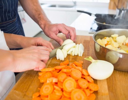 A cozy kitchen scene showing only hands of a couple preparing food, chopping vegetables, and