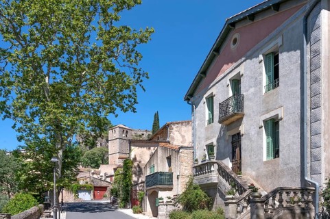 The sunlit village street of Moureze is lined with traditional stone houses with reddish-brown