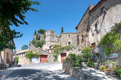 The sunlit village street of Moureze is lined with traditional stone houses with reddish-brown