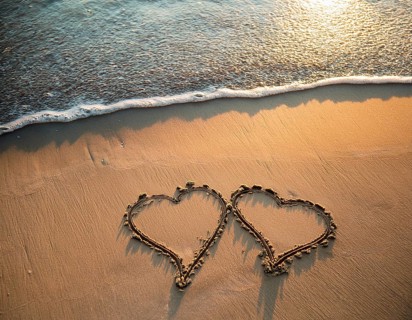 Warm tropical beach with two hearts drawn on the sand, blue waters, and clear skies, invoking