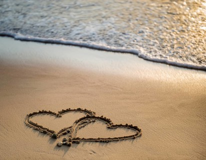 Warm tropical beach with two hearts drawn on the sand, blue waters, and clear skies, invoking