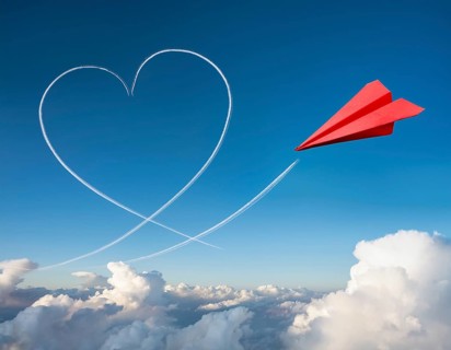 A red paper airplane depicted in flight with an artistic heart-shaped trail. The blue sky