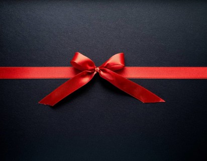 A beautifully wrapped gift box adorned with red satin ribbons forming a bow, contrasting against a
