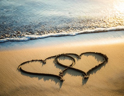 Warm tropical beach with two hearts drawn on the sand, blue waters, and clear skies, invoking