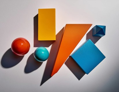 Vividly colored geometric shapes, including spheres and pyramids, artfully arranged on a surface.