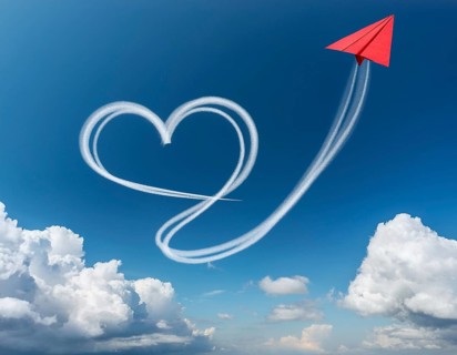 A red paper airplane depicted in flight with an artistic heart-shaped trail. The blue sky
