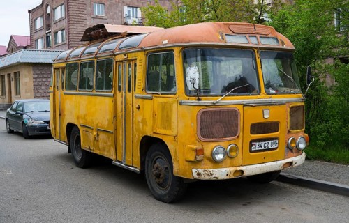 An old yellow bus stands abandoned on the street in an urban environment, clear signs of use,