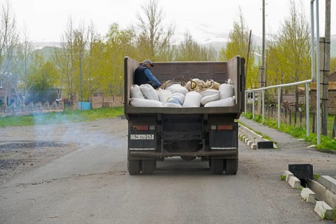 A lorry full of sacks is driven along a city street by a man in the back, exhaust fumes, Armenia