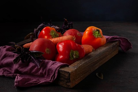 Peppers, tomatoes, carrots lie in a wooden box dark photo