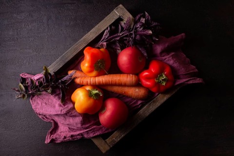 Orange and red vegetables on a red napkin in a wooden box dark photo