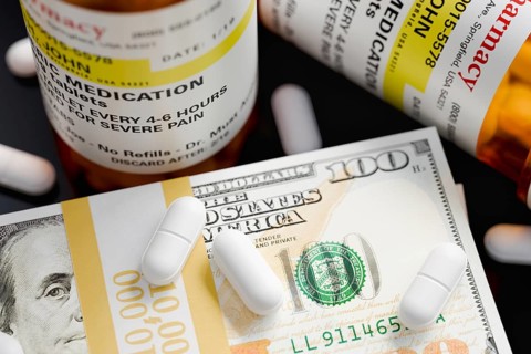 Prescription medicine bottles and pills next to stacks of 100 dollar bills