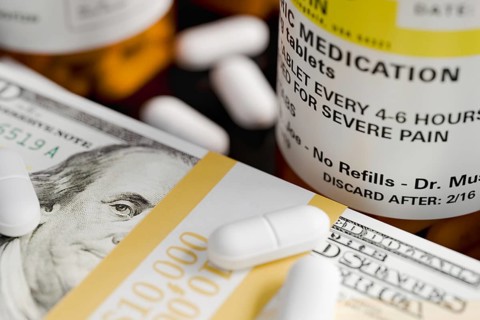 Prescription medicine bottles and pills next to stacks of 100 dollar bills