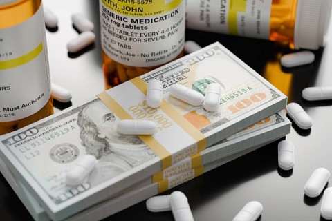 Prescription medicine bottles and pills next to stacks of 100 dollar bills