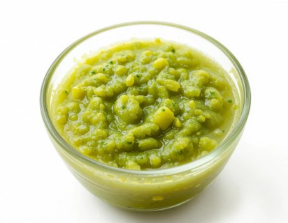 A clear glass bowl holds a thick, textured pea soup, showcasing a fresh, healthy meal. The bright