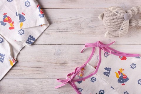 Clothes for a newborn and a rattle on a white wooden background