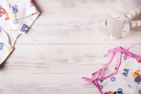 Clothes for a newborn and a rattle on a white wooden background