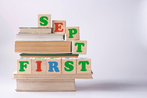 Wooden cubes with the inscription First sept stands on a stack of books copy space